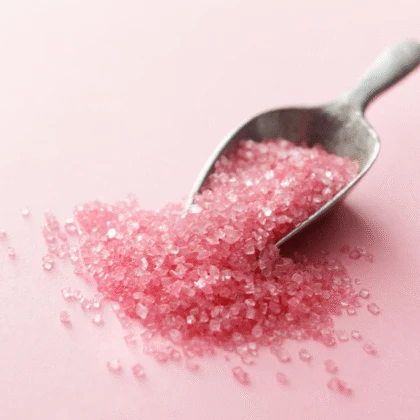 a spoon full of pink sugar on a pink background